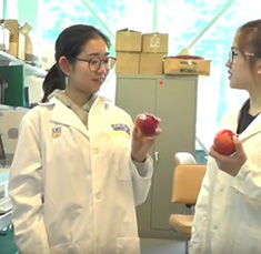 2 students wearing lab coats and holding apples